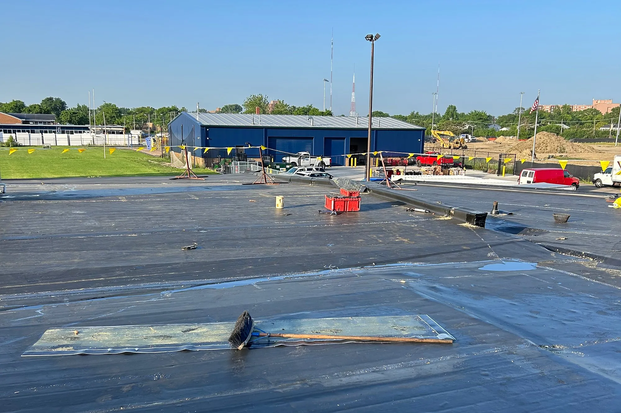 Flat membrane roof mid-replacement, with a blue district building and athletic fields beyond