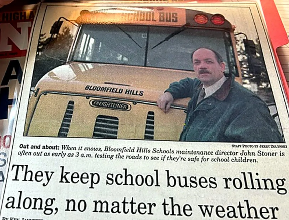 Newspaper clipping showing John Stoner beside a Bloomfield Hills school bus, headlined “They keep school buses rolling along, no matter the weather”