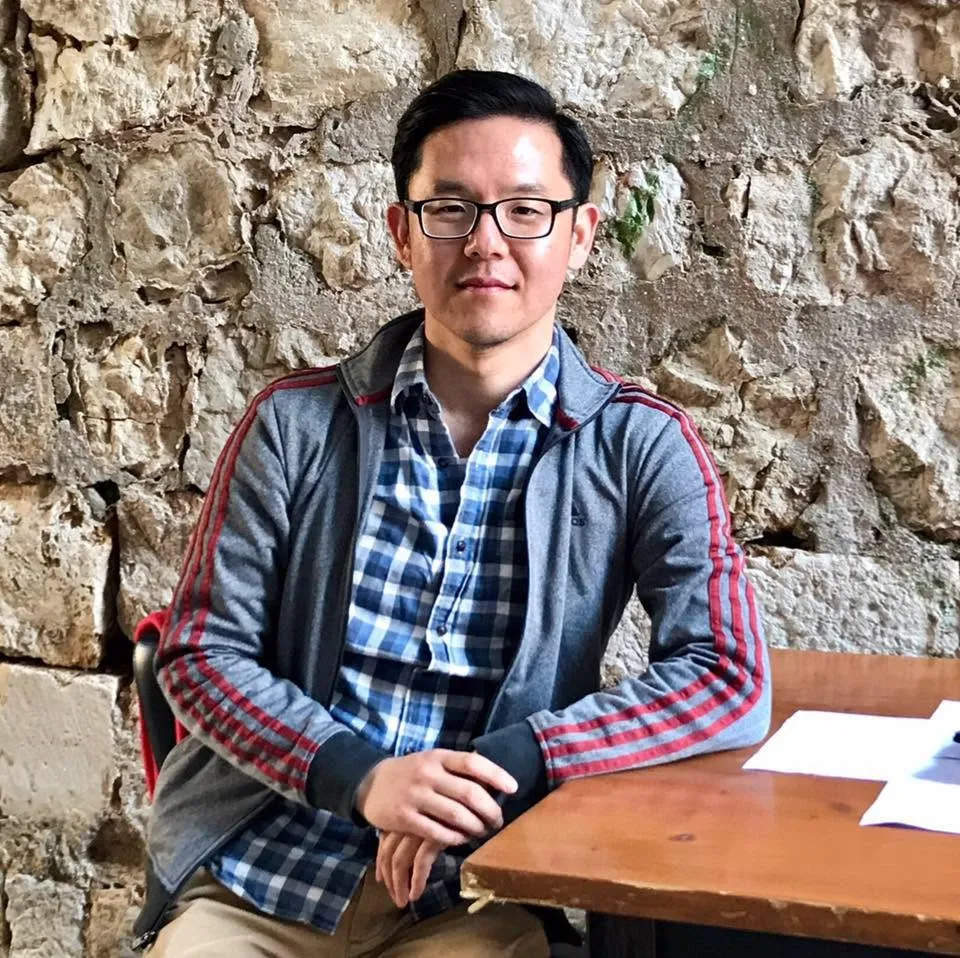 Youn Kim, in glasses, a plaid shirt and a gray track jacket